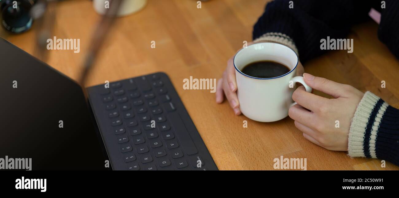 Side view of female hands holding coffee cup on wooden worktable with ...
