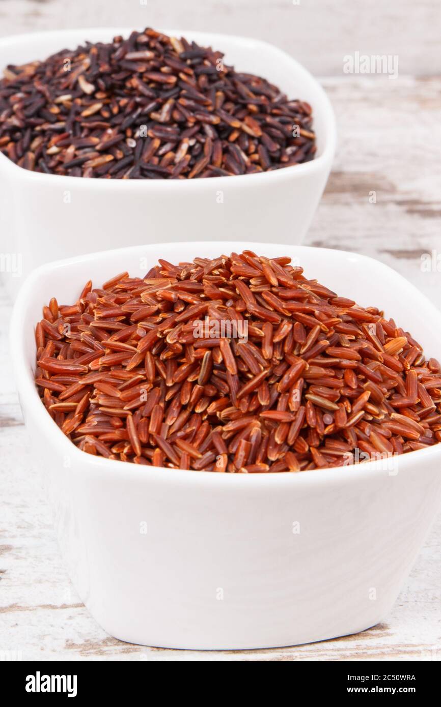 Black and red rice in white glass bowls on rustic board, concept of ...