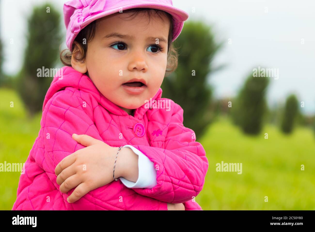 a stubborn 2-year-old girl embracing herself in a park on an overcast day Stock Photo