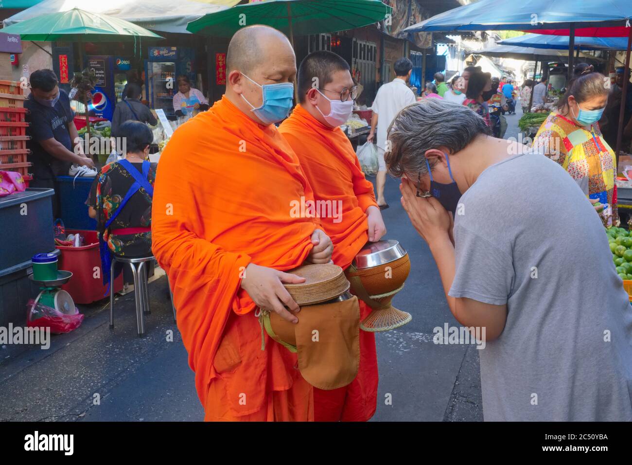 Two Buddhist monks wearing anti-Covid masks are reverently greeted during their daily alms round (binta baat) in a market in Bangkok, Thailand Stock Photo