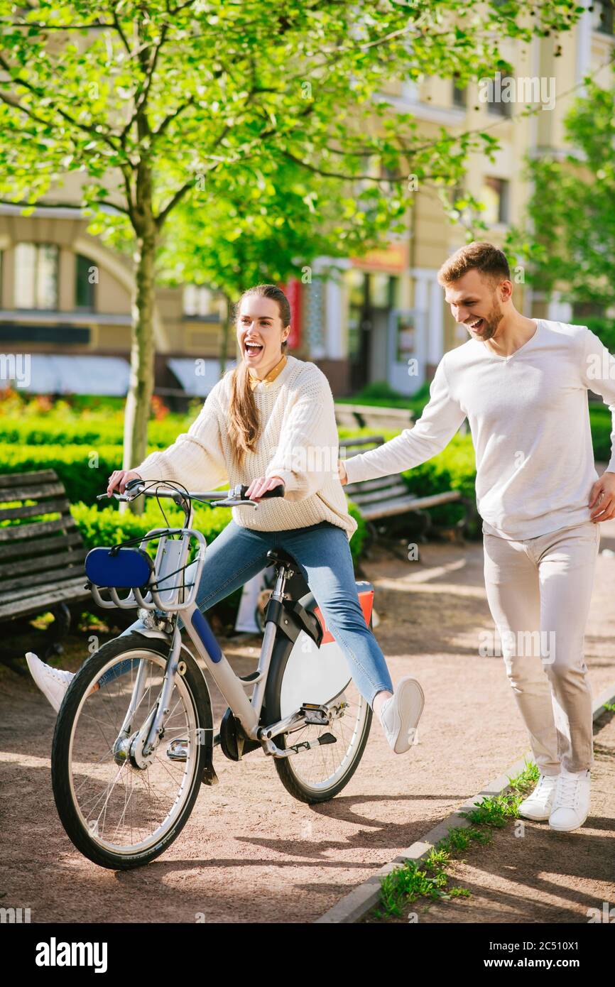 Cheerful woman on bicycle and attentive man running nearby Stock Photo
