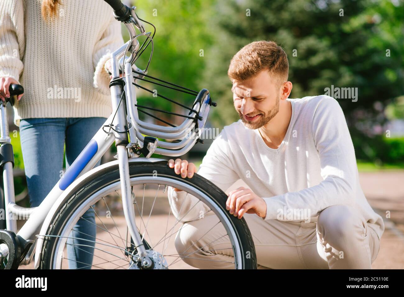 Bearded guy looking at wheel and woman supporting bike Stock Photo - Alamy