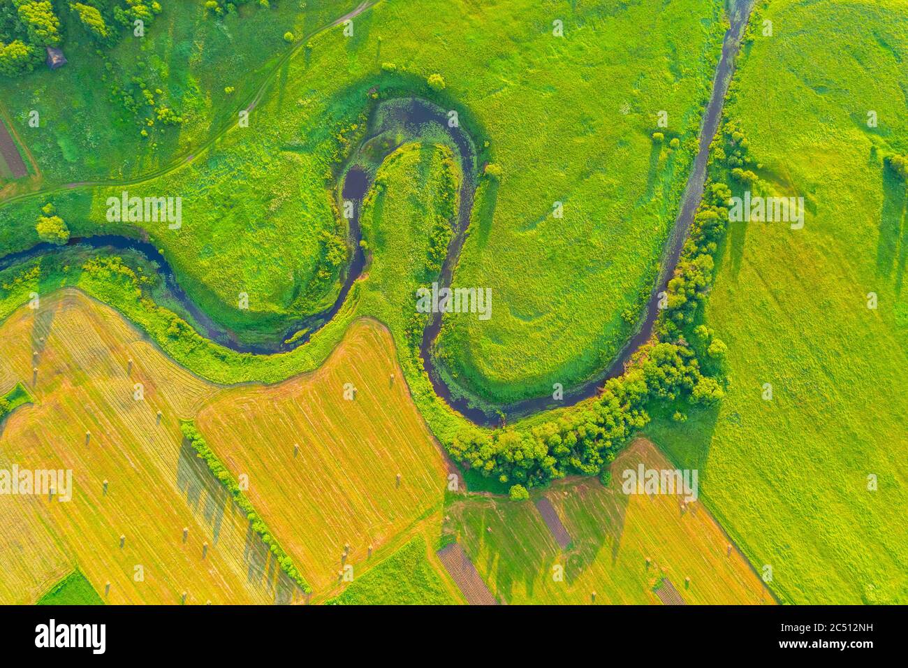 Top aerial view of the natural landscape valley of a meandering river among green fields and forests Stock Photo