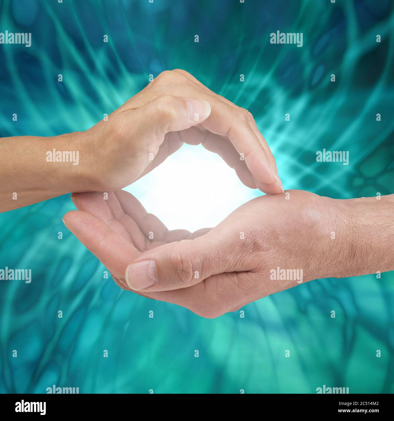 Our combined energy creates an unbeatable healing power - female hand cupped above male cupped hand with bright white light between against a jade Stock Photo
