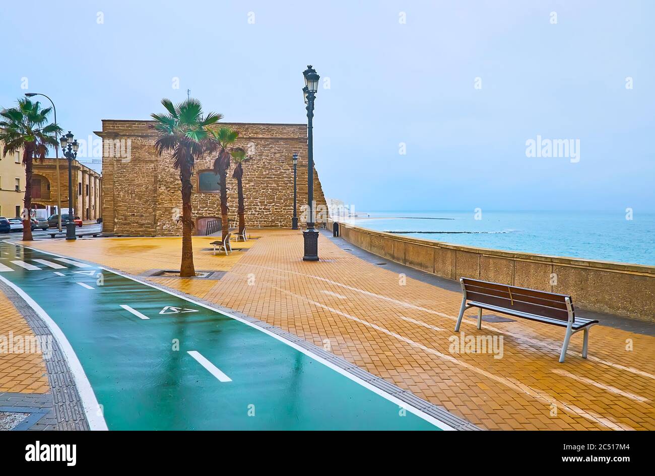 The rainy morning on Atlantic Ocean shore with a view on Baluarte de San Roque (bastion) of Cadiz fortress, foggy rainy sky and stormy waters, Spain Stock Photo