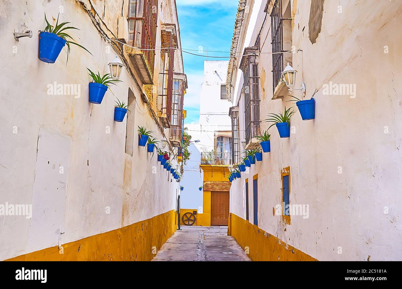 The narrow backstreet in old town, decorated with plants in blue pots, hanging on the houses walls, Sanlucar, Spain Stock Photo