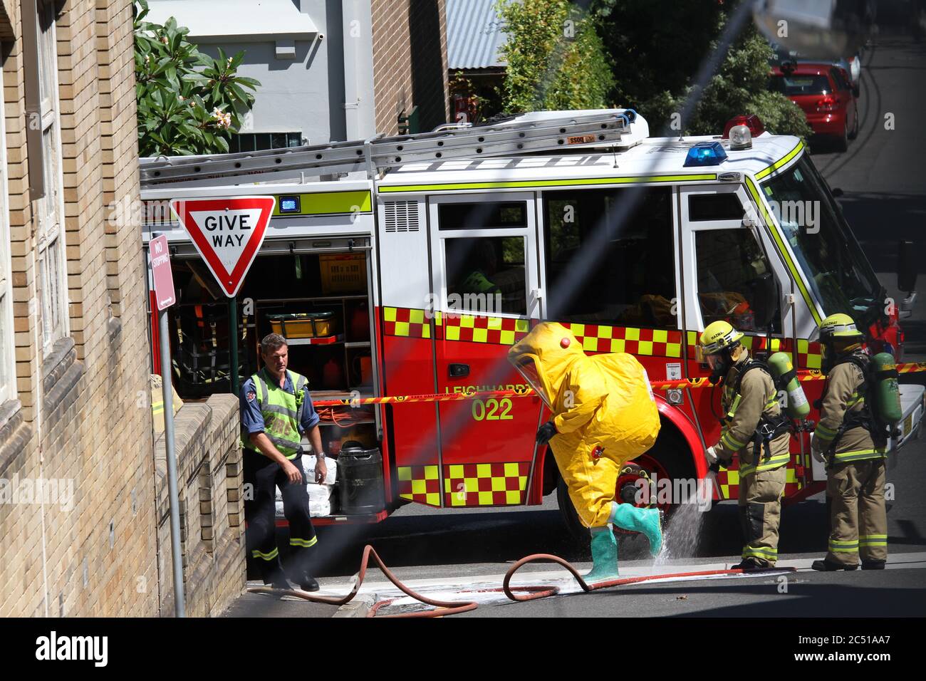 The NSW Fire Brigades workers in yellow hazardous materials protective clothing are washed clean at the Woolley Street end of St James Lane in Glebe. Stock Photo