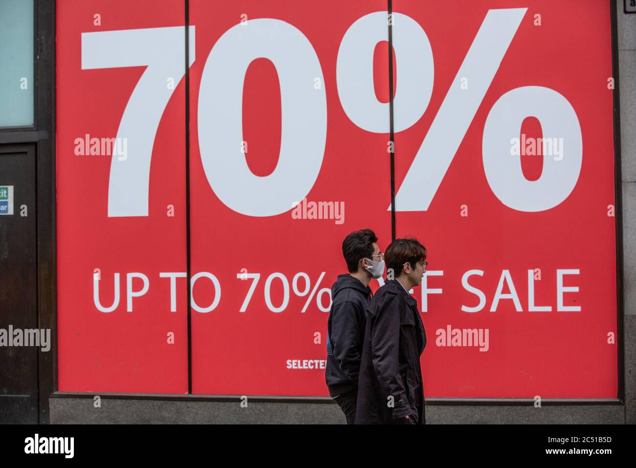 Shoppers wearing face masks walk past a large shop window advertising 70% sale reduction on Oxford Street, West End, London, UK Stock Photo