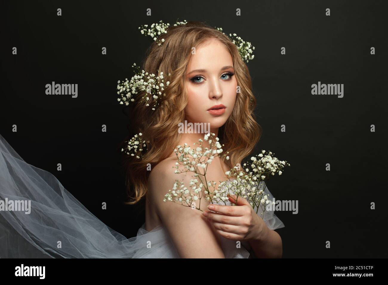 Fiancee girl with long healthy curly hair and white flowers on black background Stock Photo