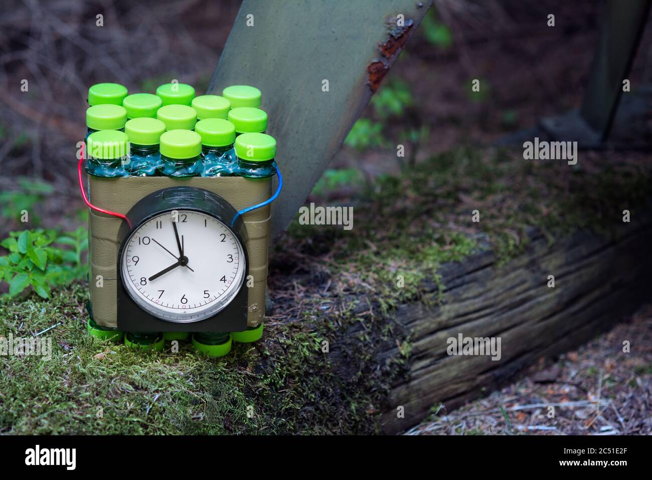 Improvised time bomb planted near metal part on old wood with green moss. Dangerous explosive device. Violent crime, terrorist act or military attack. Stock Photo