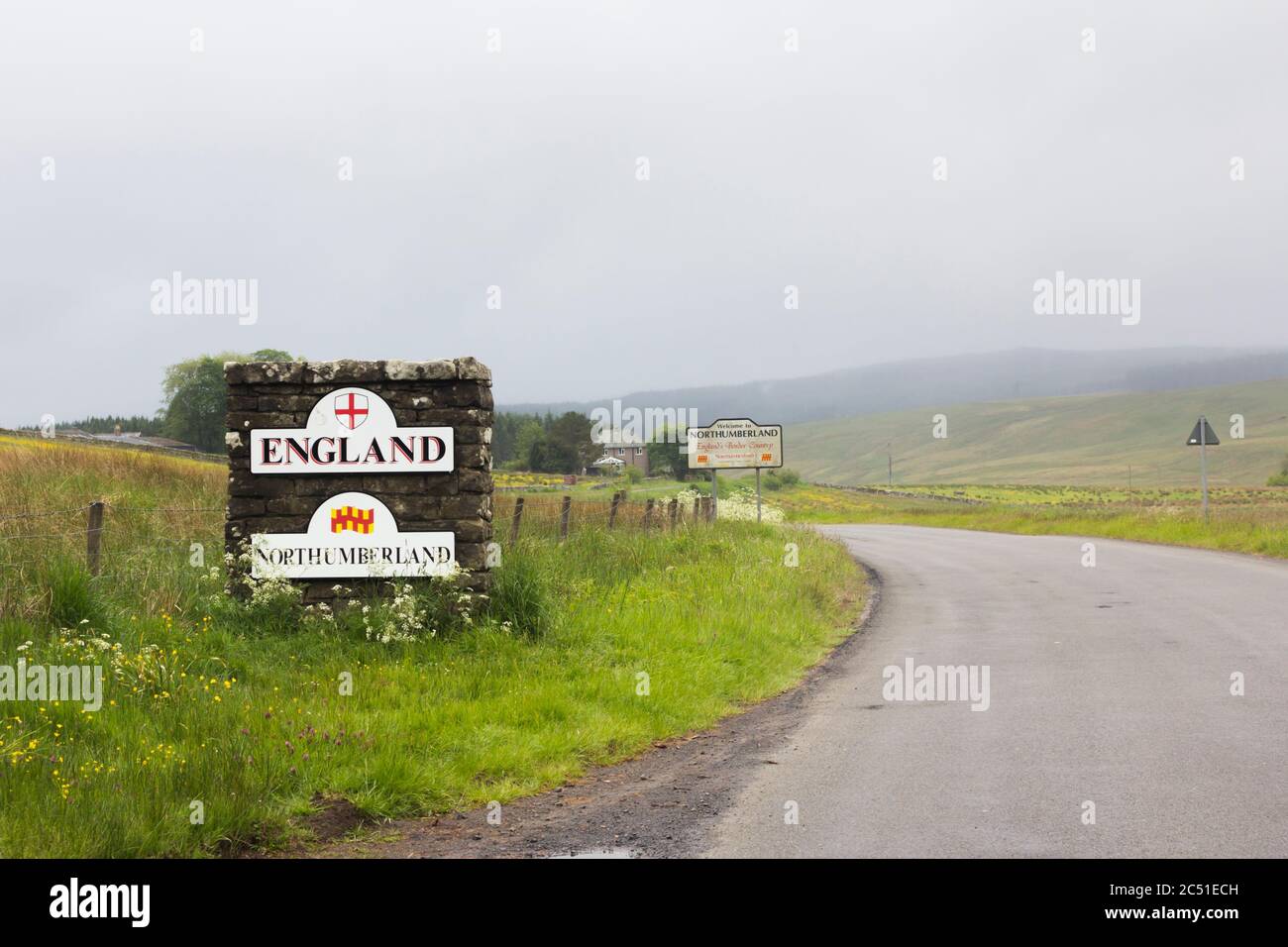 Stone pillar and signs marking the England/Scotland border near on an unclassified road at Deadwater,Kielder, Northumberland on a dull & misty day. Stock Photo