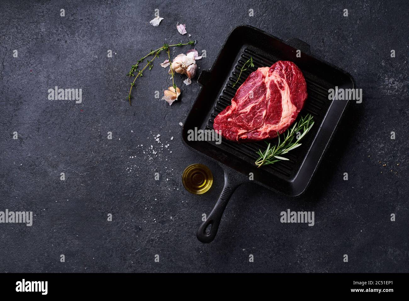 Top view Black Angus prime beef chuck roll  steak on cast iron grill pan with fresh rosemary, thyme, olive oil, garlic and spices. Creative layout wit Stock Photo