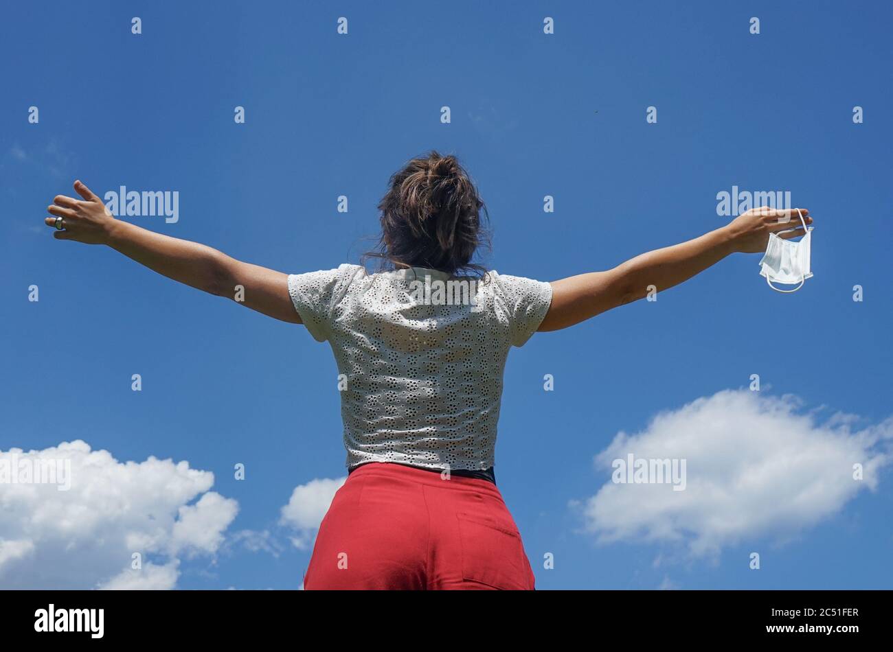Woman with arms outstretched to the sky with protective mask in hand. Concept of end of coronavirus pandemic and freedom found. Vivid colors. Stock Photo