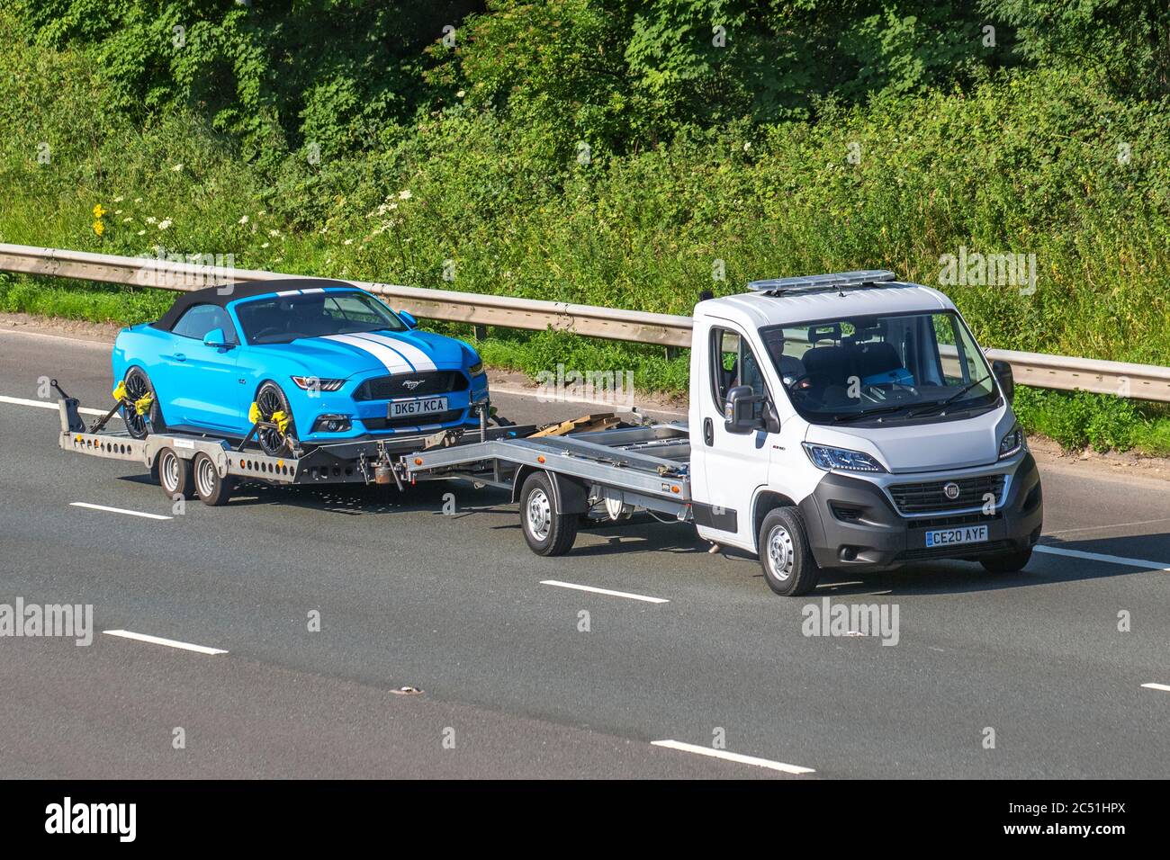 2017 blue white Ford Mustang GT V8 towed by new 2020 white Fiat Ducato 2.3 130bhp Recovery Truck Car Transporter Euro 6;  Vehicular traffic on tow, moving vehicles, cars driving vehicle towing car trailer on UK roads, motors, motoring on the M6 motorway Stock Photo