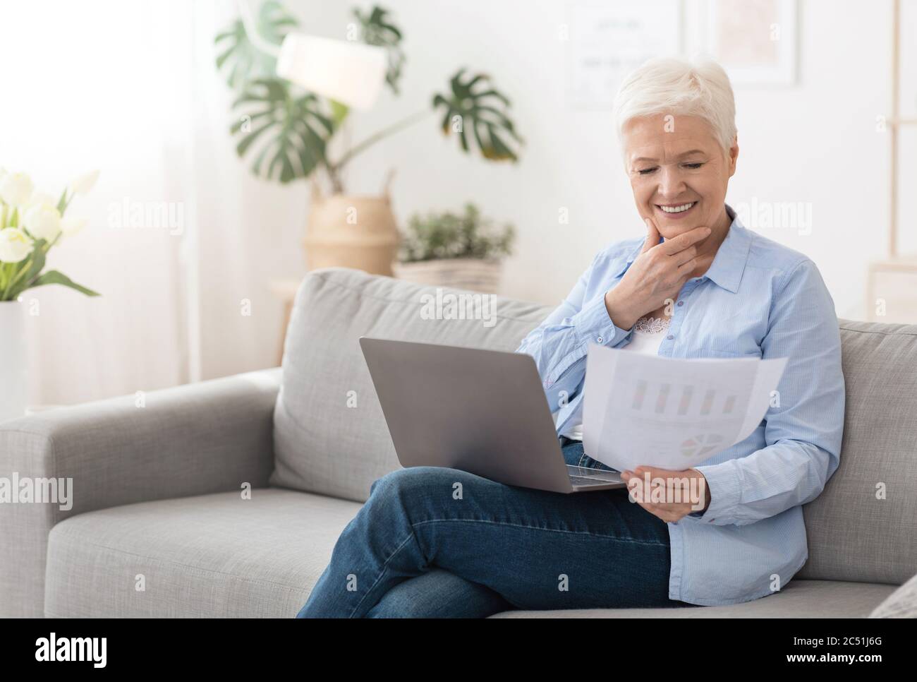 Senior woman using laptop and reading documents while working remotely at home Stock Photo