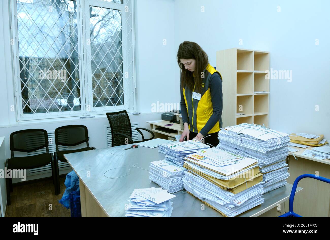 At the post office, sorting room: female postal worker in uniform sorting letters and parcels standing at the work table Stock Photo