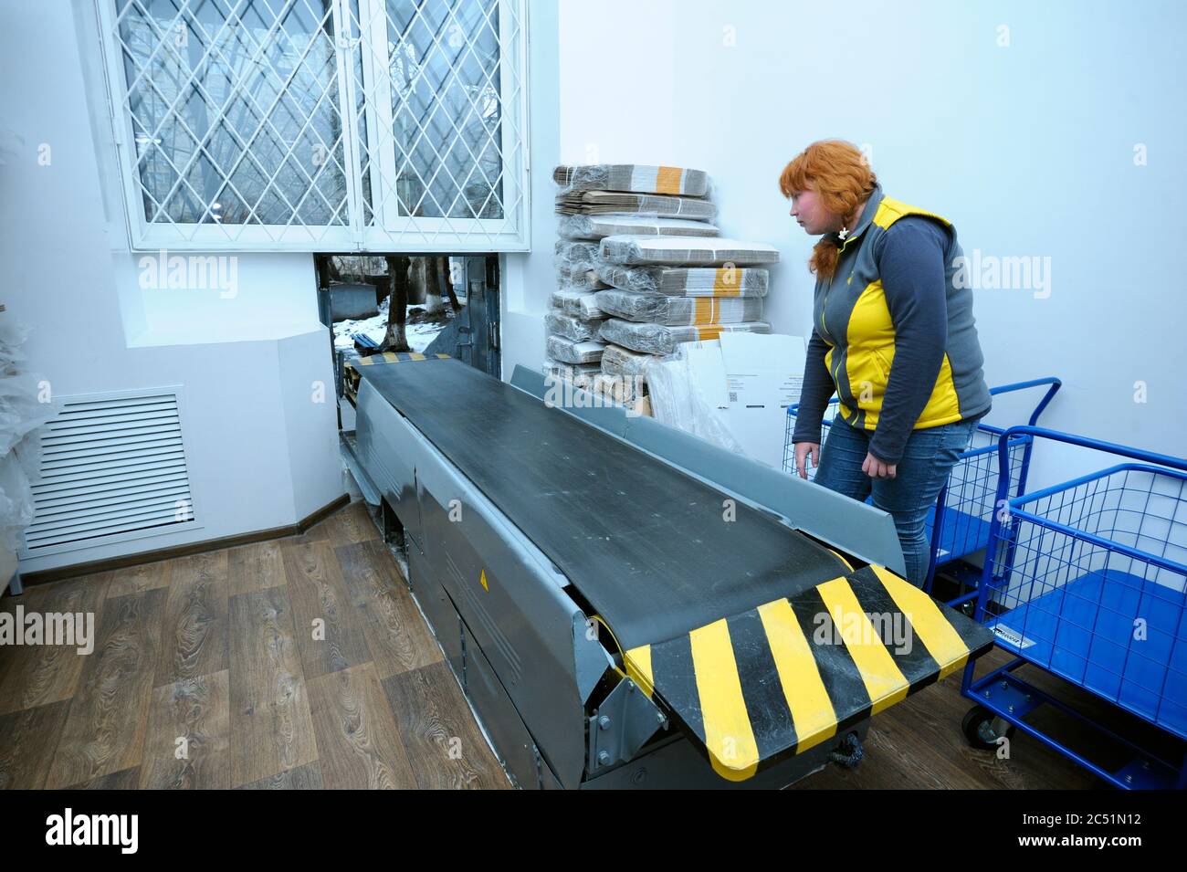 At the receipt and delivery room of post office: postal worker standing by a belt conveyor Stock Photo