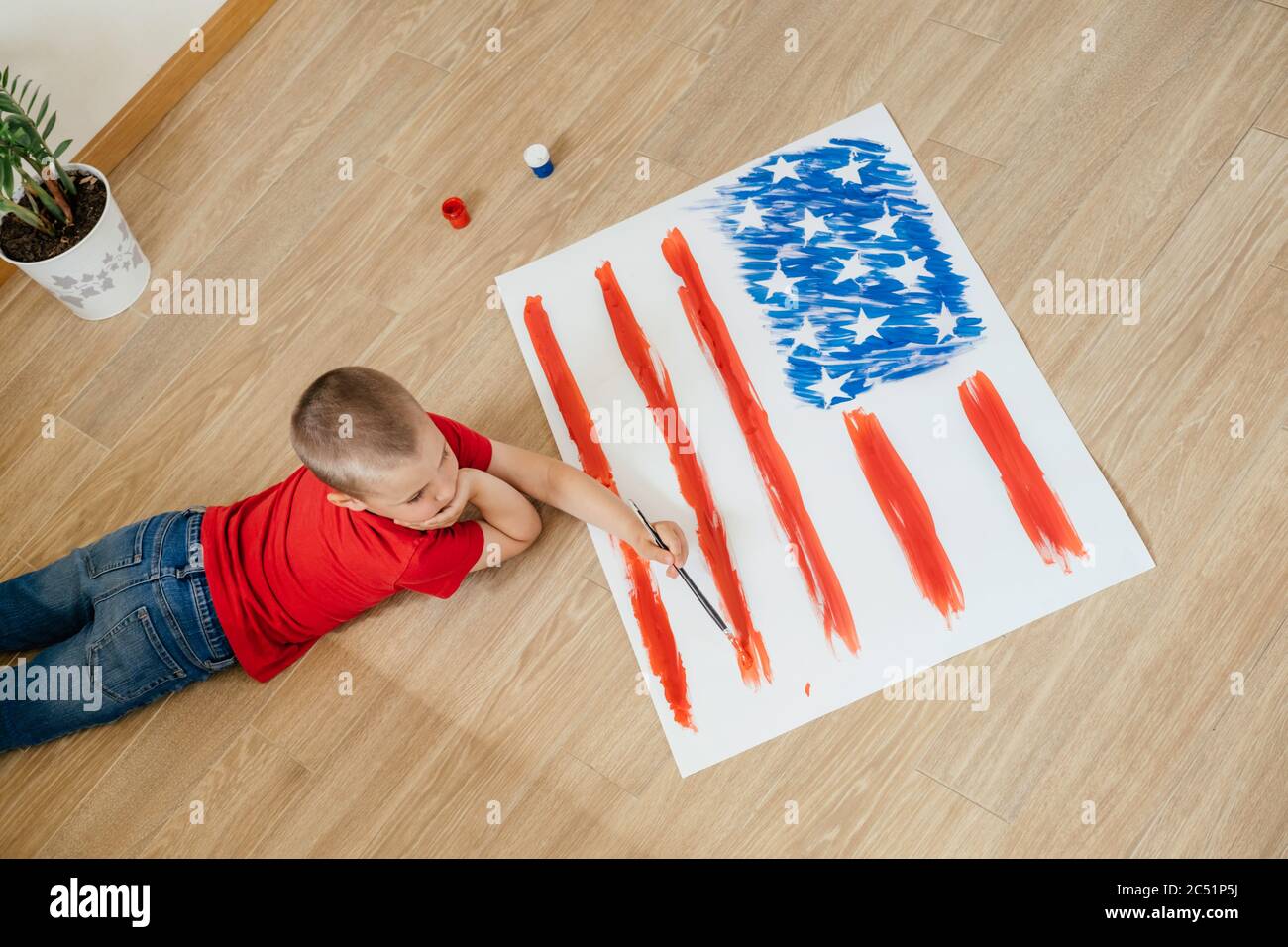 The Young Boy In A Red T Shirt And Blue Jeans Laying On The Floor And Drawing With A Brush The Flag Of America Concept Of Independence Day July 4 Stock Photo