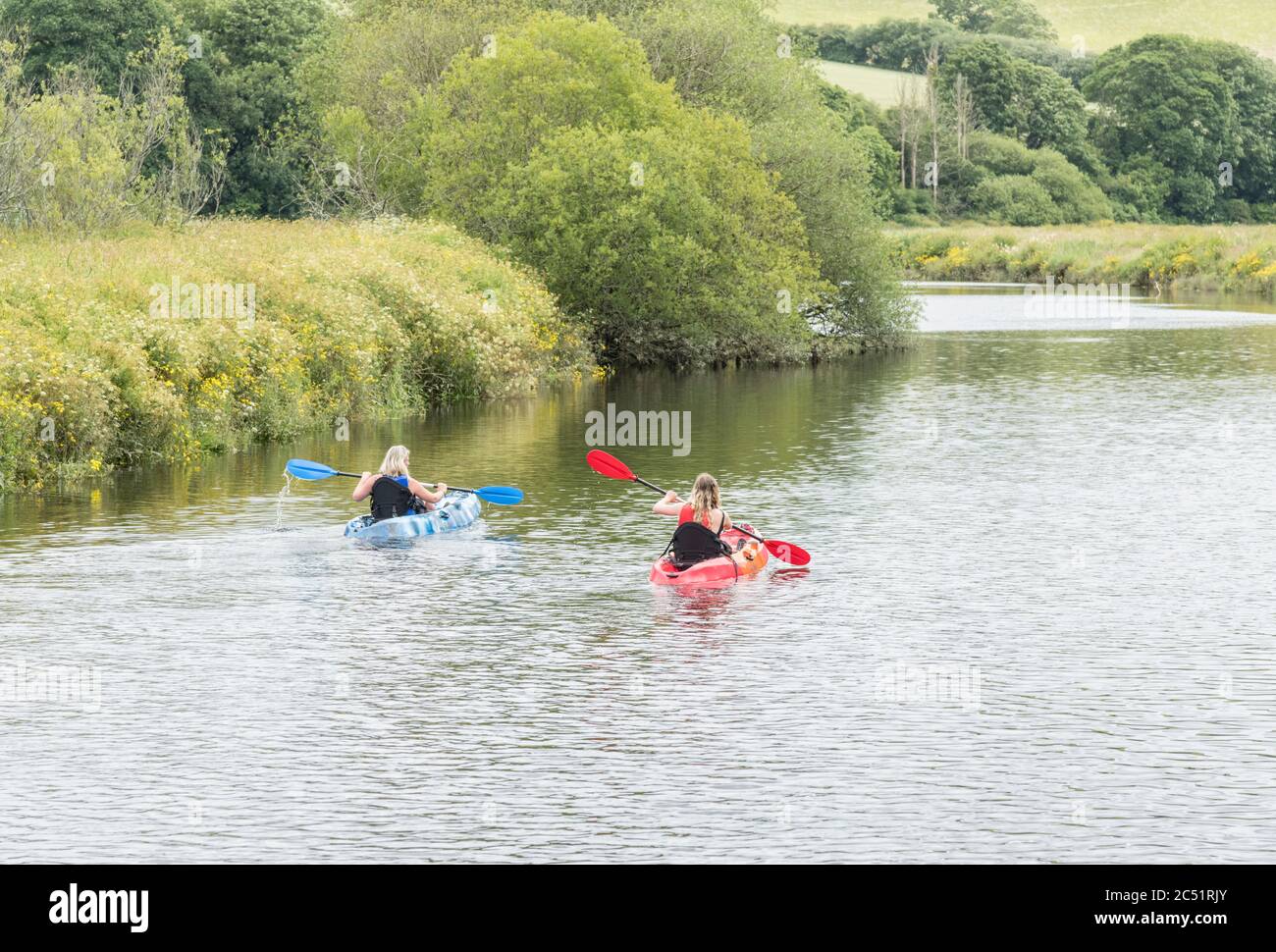Two female canoeists / kayakers paddling on the River Fowey at Lostwithiel in Cornwall. Heading downstream. Stock Photo