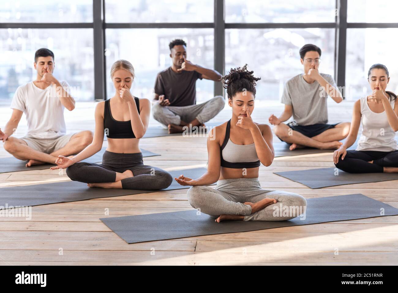 Young men and women in yoga studio practicing alternate nostril breathing exercises Stock Photo