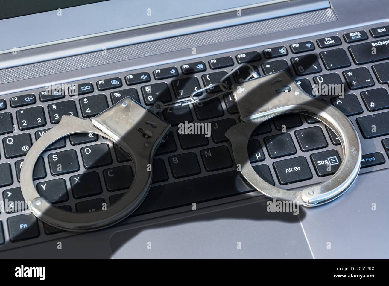 Handcuffs lying on a computer keyboard plus dark shadow of a hand symbolizing cyber crime Stock Photo