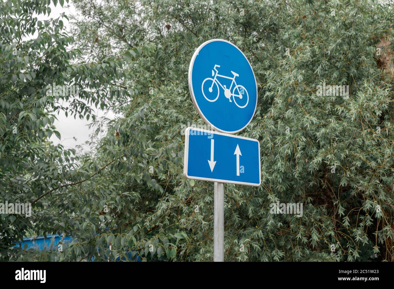Two way bicycle lane sign against green tree top Stock Photo