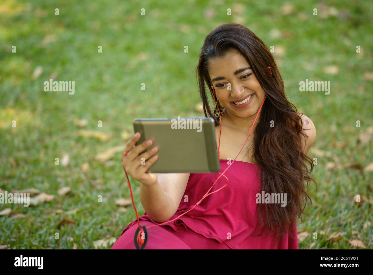 Happy young beautiful Indian woman using digital tablet at the park ...