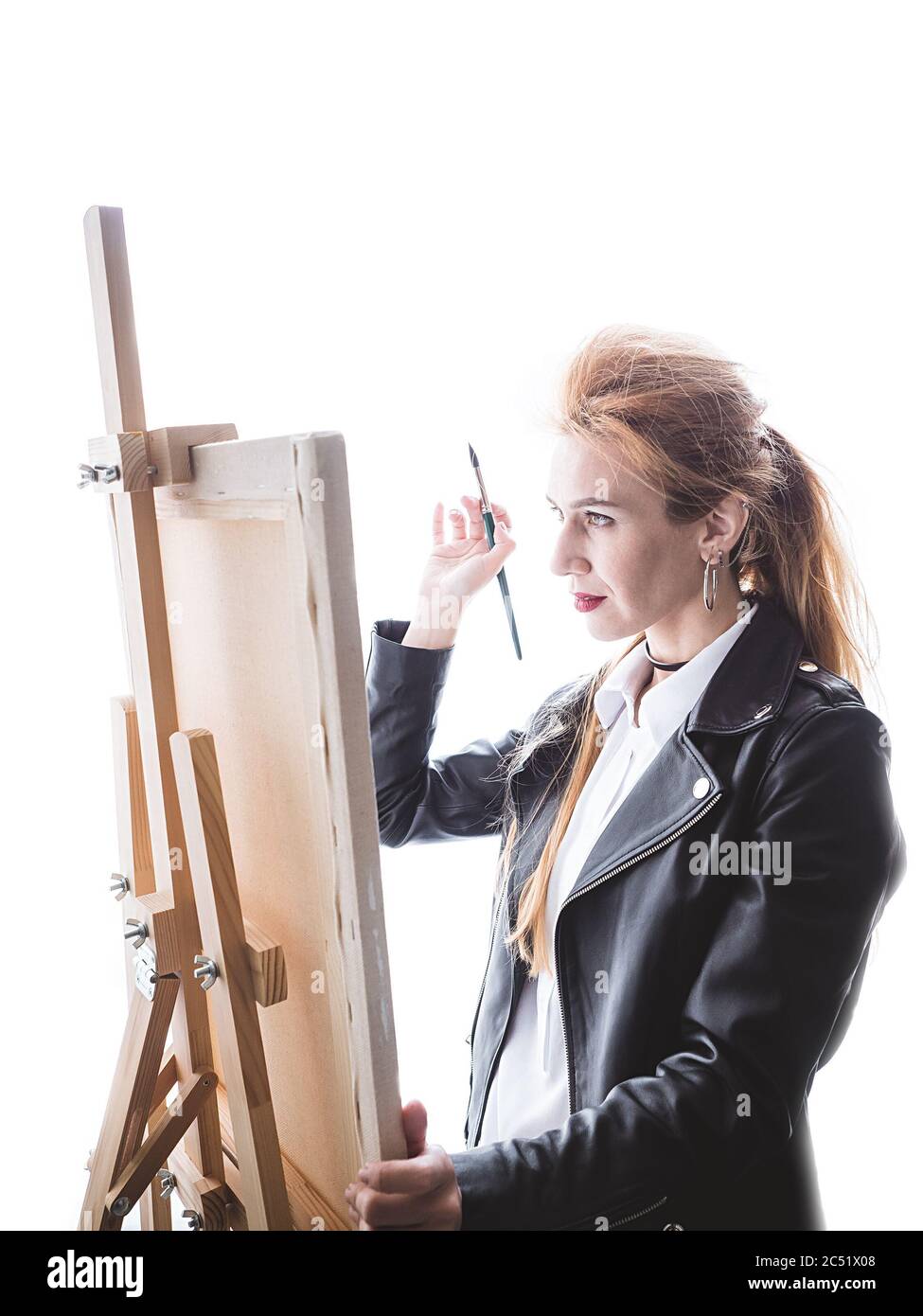 Beautiful girl artist stands in front of easel with a brush on a bright ...