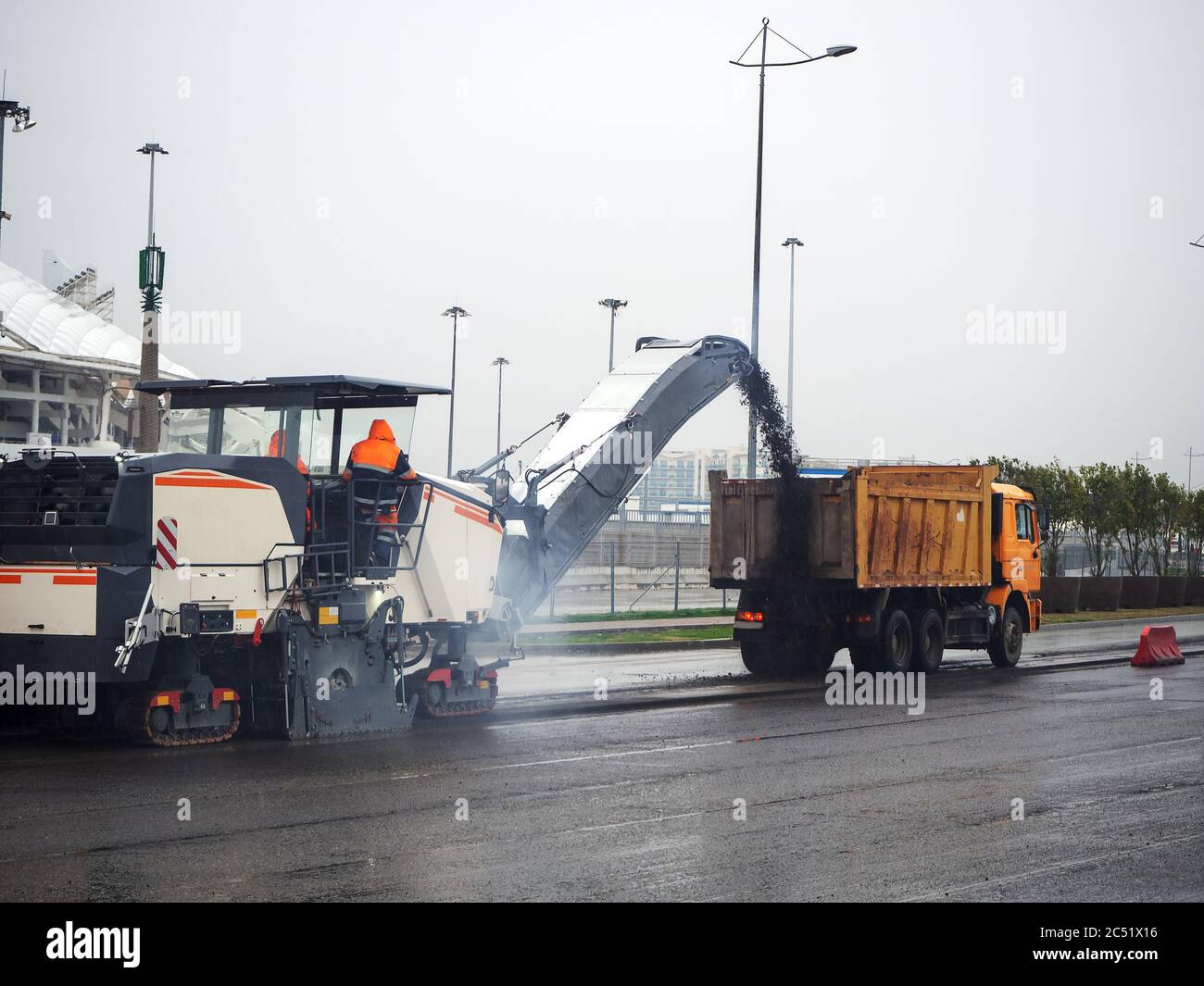 Road mill loads crushed asphalt into a dump truck on a gray cloudy day Stock Photo