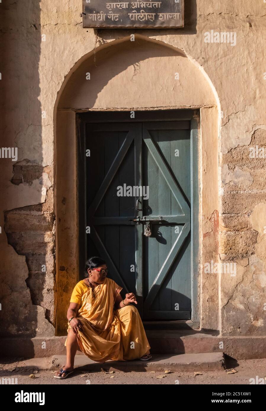 Nagpur, Maharahstra, India - March 2019: An Indian woman sitting alone under an old door on the streets of the city. Stock Photo