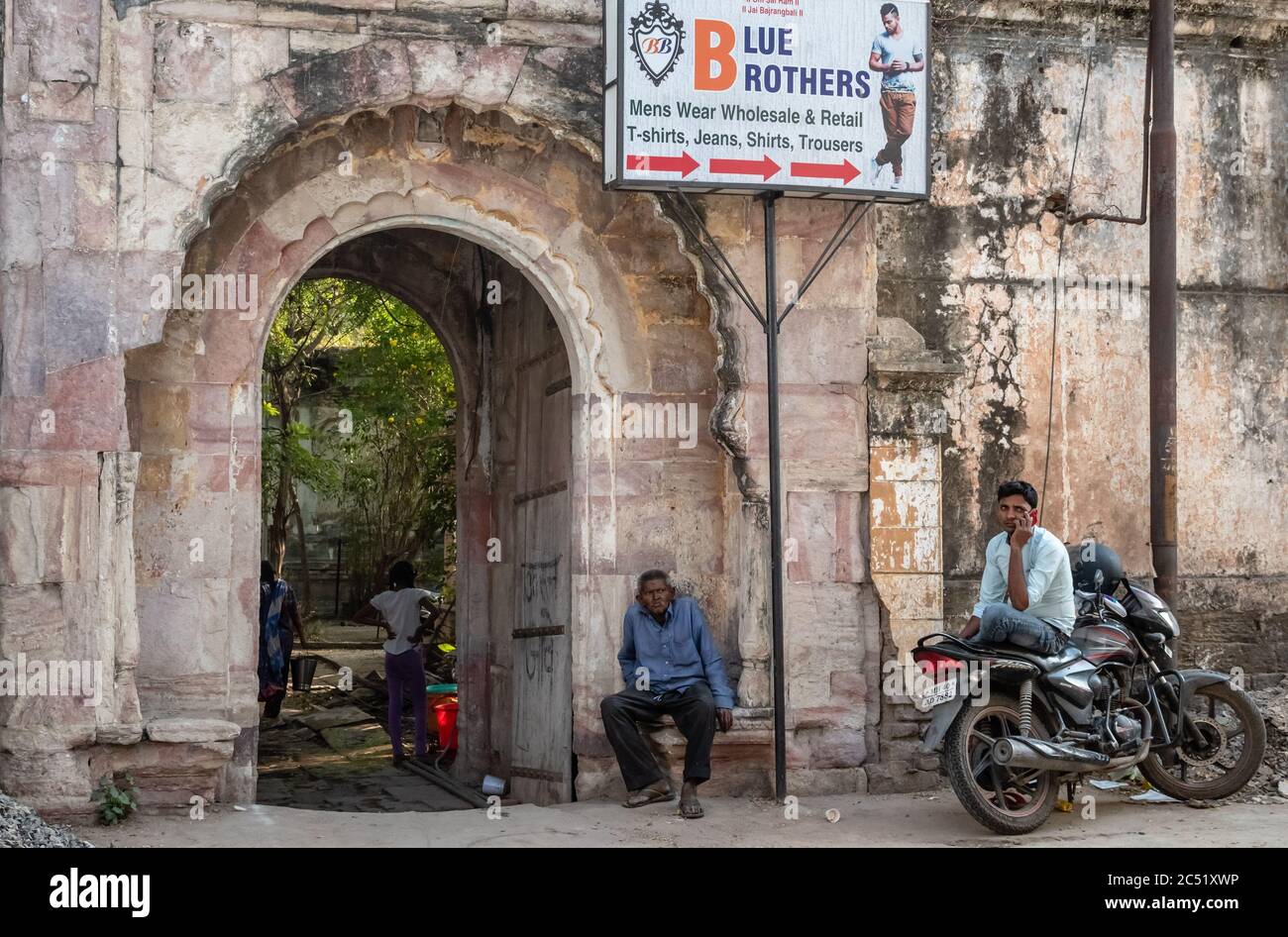 Nagpur, Maharashtra, India - March 2019: Indian men sit beneath the old arches of an ancient stone gateway in the old city of Nagpur. Stock Photo