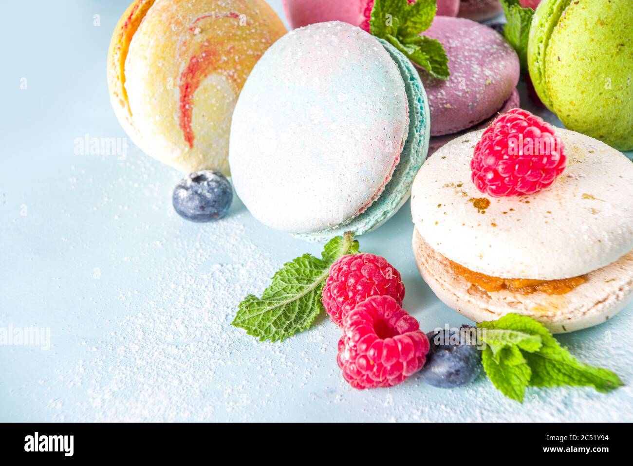 Colorful french macaron dessert. Set of various different tastes and color macaron cookies with berries, sugar powder and mint on blue background Stock Photo