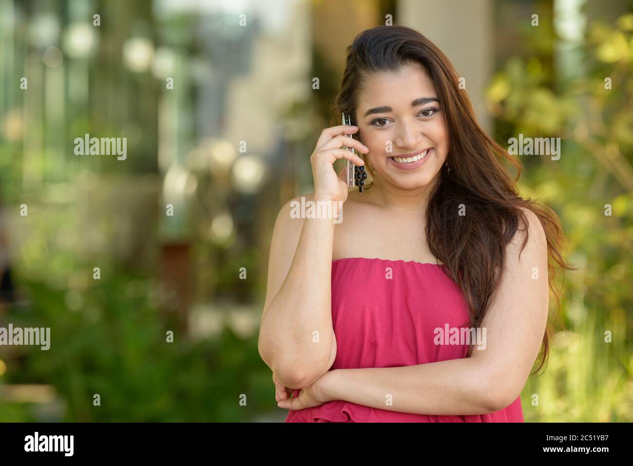 Happy young beautiful Indian woman talking on the phone at the park ...