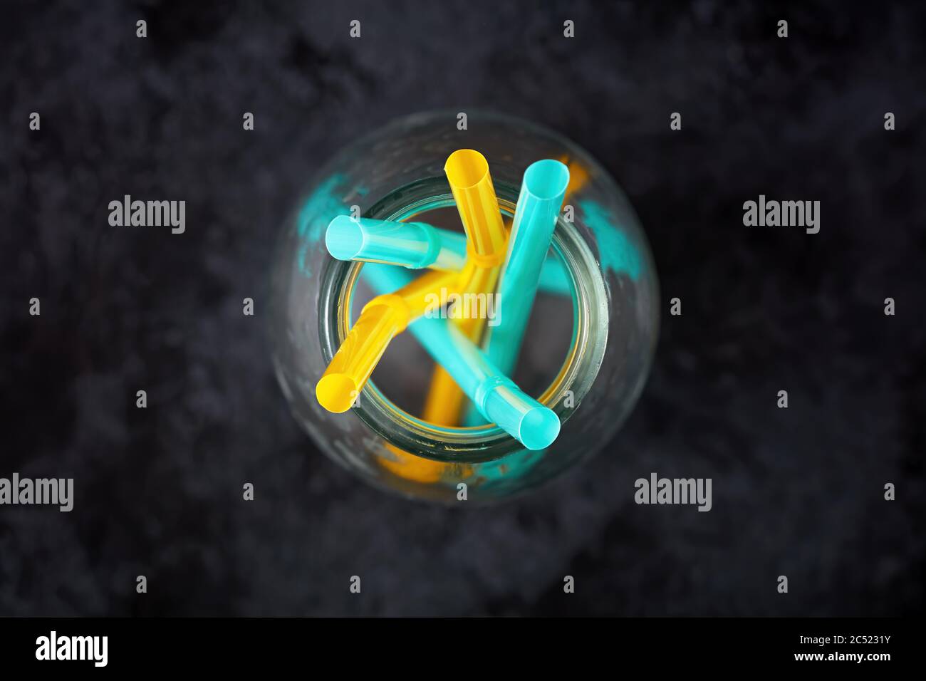 Yellow and blue plastic straws in an empty glass bottle on black