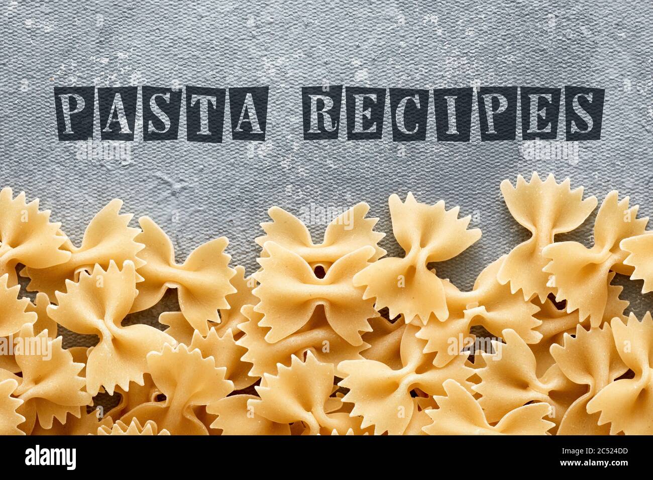 Template for pasta recipe with raw farfalle on textured gray background. Overhead view. Stock Photo