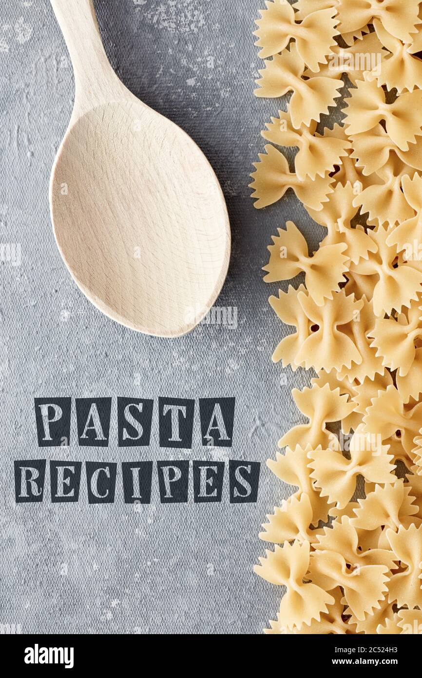 Template for pasta recipe with raw farfalle and wooden spoon on textured gray background. Overhead view. Stock Photo