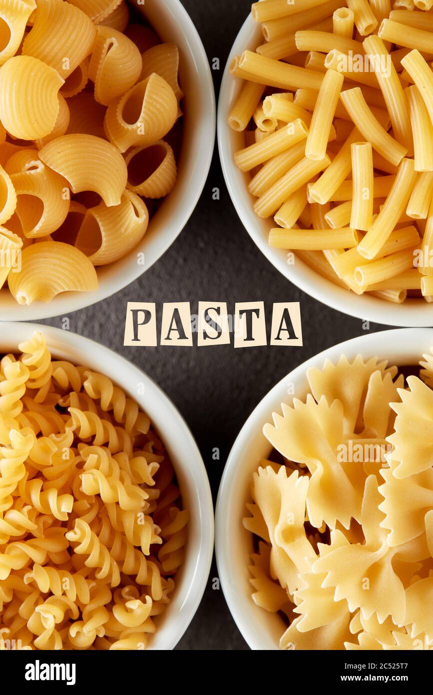 Template for pasta recipe with various raw pasta in white bowls. Overhead view with text. Stock Photo