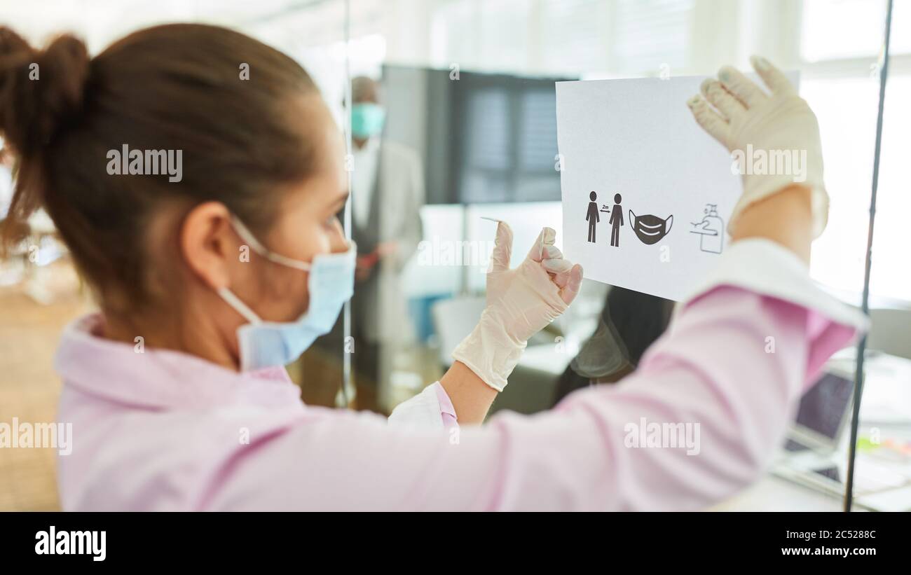 Businesswoman picks up a notice in the office with hygiene rules for infection control because of Covid-19 Stock Photo