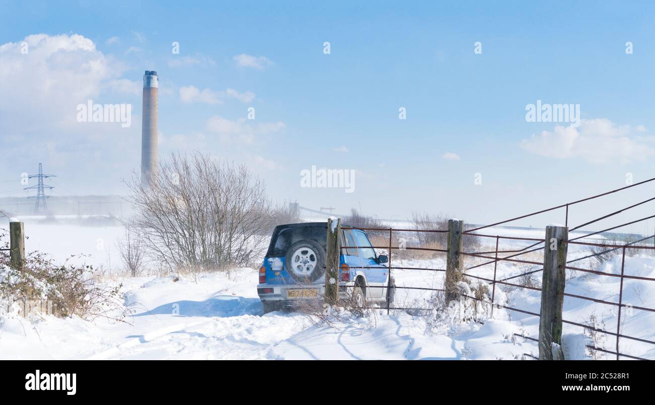 A 4x4 off roader, stuck in the deep wintry snow, on the sea wall of the river medway. During storm Emma, kingsnorth powerstation in the background. Stock Photo