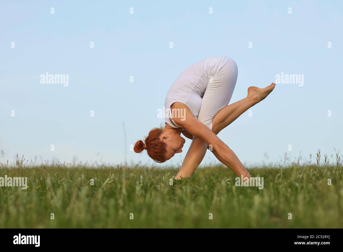 Yoga balance in nature. Concentrated young woman practicing morning yoga on meadow. Beautiful girl doing forward bend exercise outdoors Stock Photo