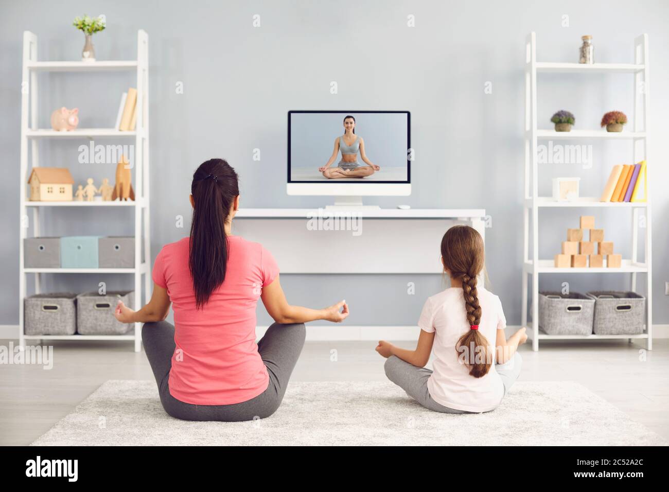 Back view of mother and daughter doing yoga to online video tutorial at home. Parent and child meditating or exercising Stock Photo