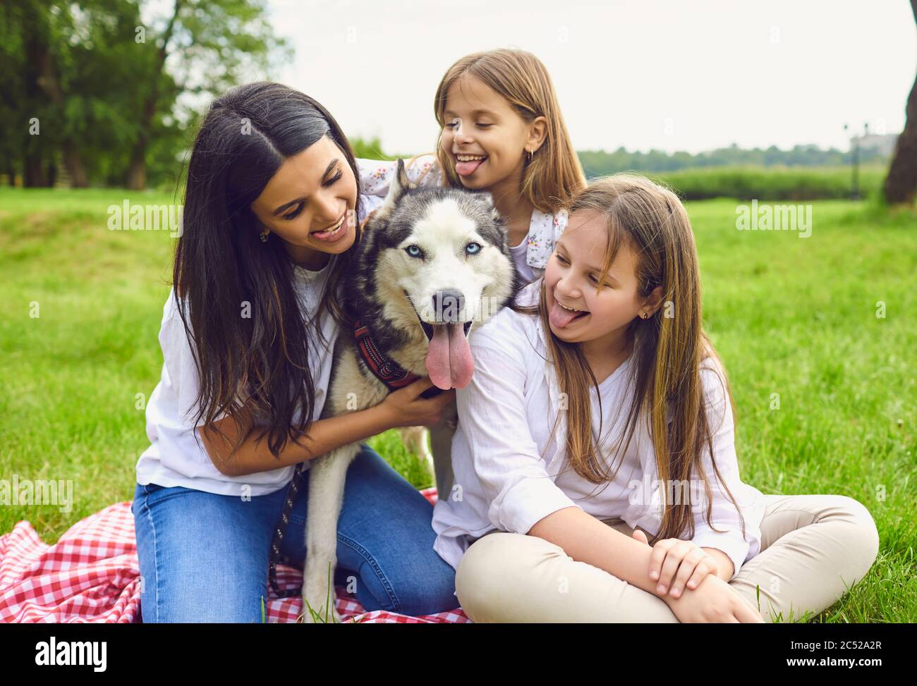 Happy family with husky dog lying on grass in summer park. Stock Photo