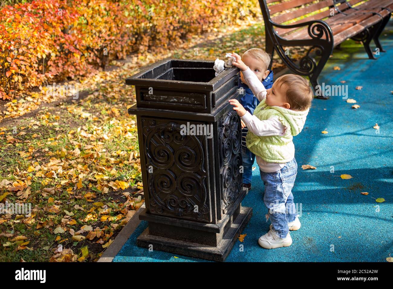smart generation concept. two little cute babies are standing near the black street container in the park and throwing garbage there. another kid Stock Photo
