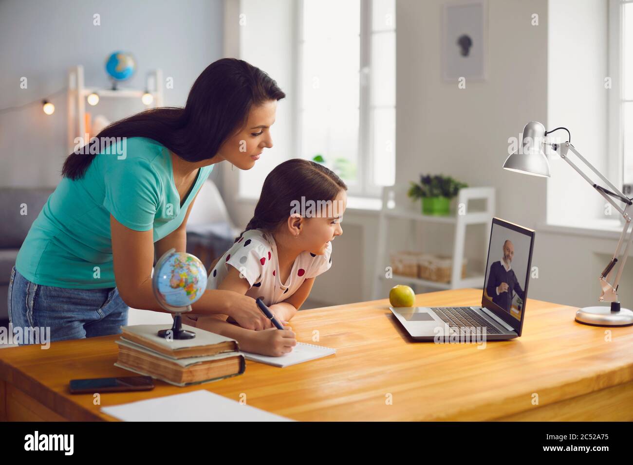 Distance education. Mother and daughter watching online video conference with mature teacher on laptop at home Stock Photo