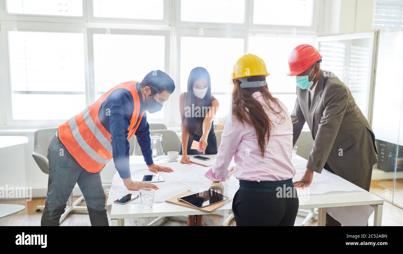Group of architects with face mask and blueprint on a table discuss a construction project Stock Photo