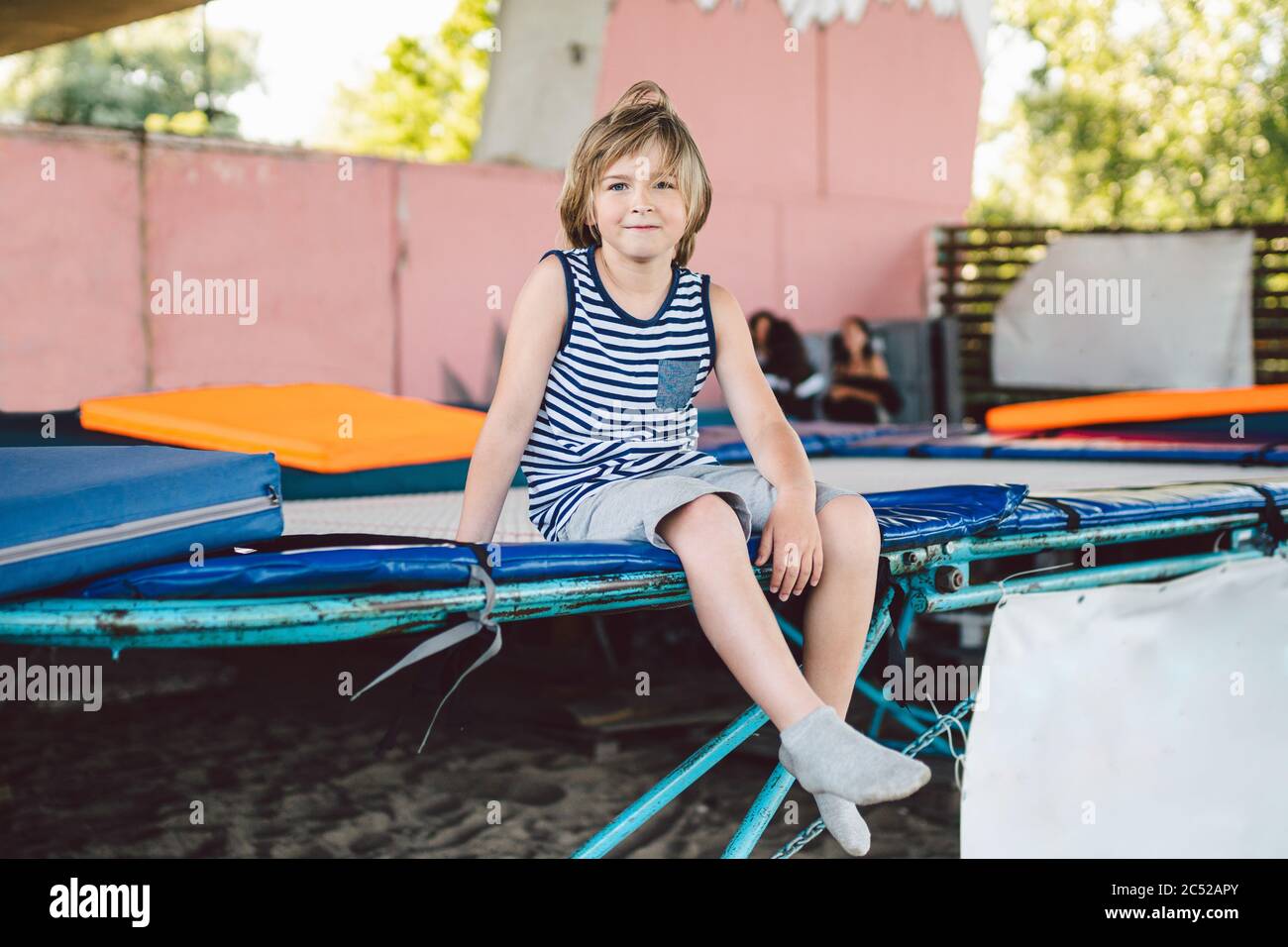 The theme of childhood, sports and health. Little boy gymnast resting in trampoline training session. A child athlete sits on a trampoline and looks Stock Photo