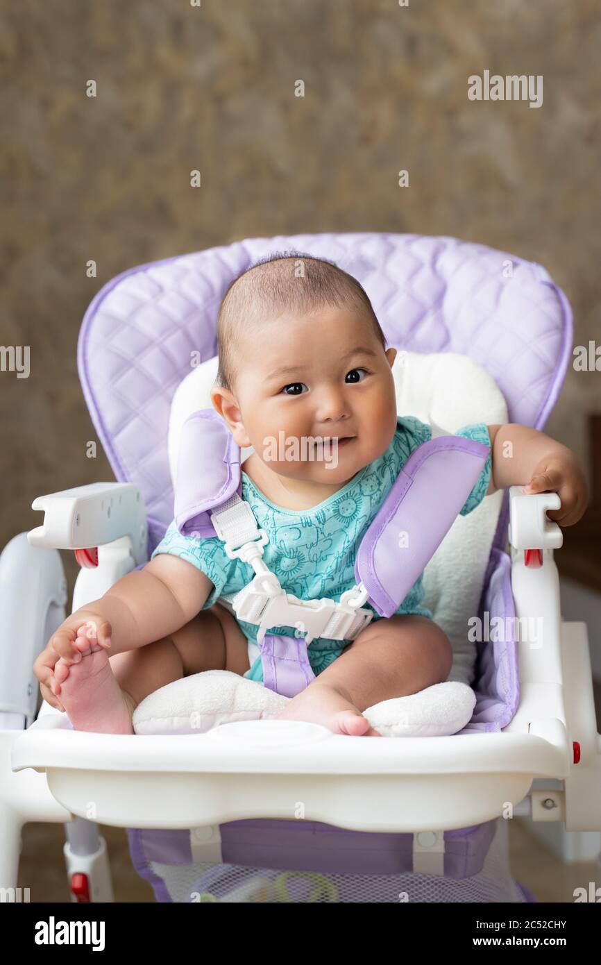 a beautiful Asian sixmonthold baby is sitting in a high chair Stock