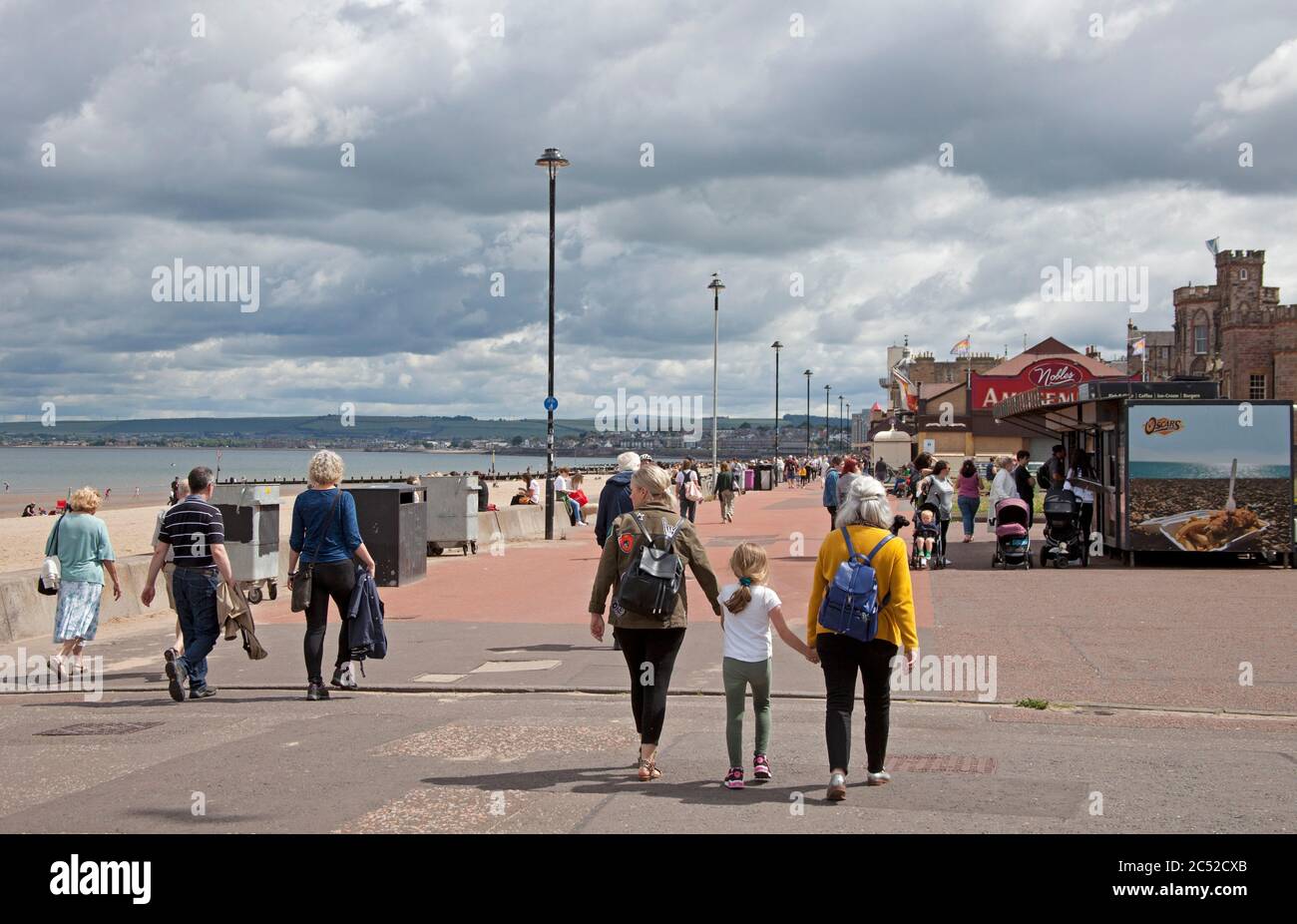 Portobello, Edinburgh, Scotland, UK. 30 June 2020. Today marks 100 days since the UK went into Lockdown due to the Covid-19 Coronavirus pandemic. Looking at Portobello seaside area it is difficult to see that anything has changed from before the shutdown, people are sitting together at tables and on the promenade wall, they are buying their coffee and snacks from the kiosks and cafes. Although the temperature was 18 degrees at lunchtime there were fewer people on the beach than on the promenade. Stock Photo
