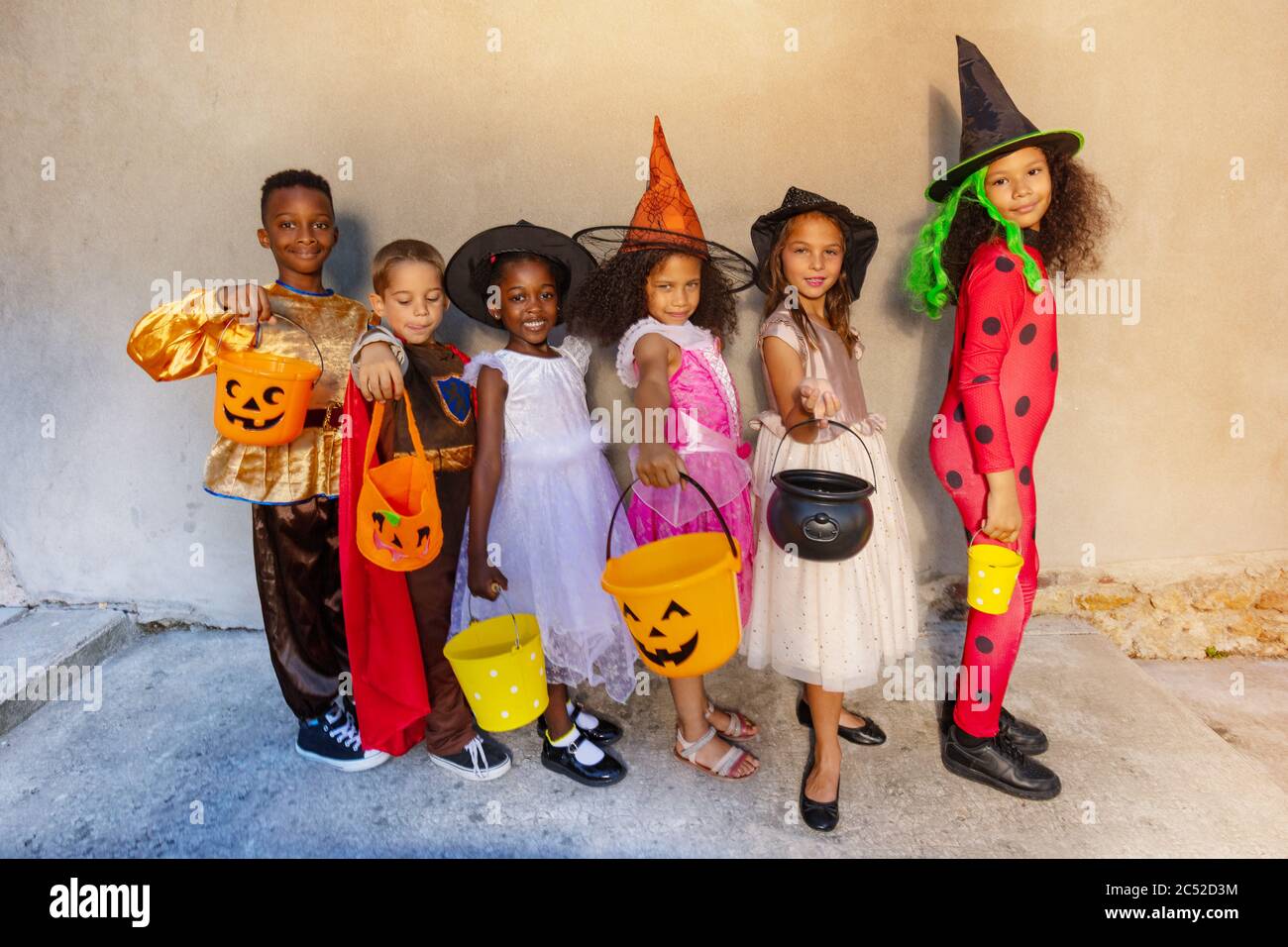 Group of kids in Halloween costumes stand together with candy buckets