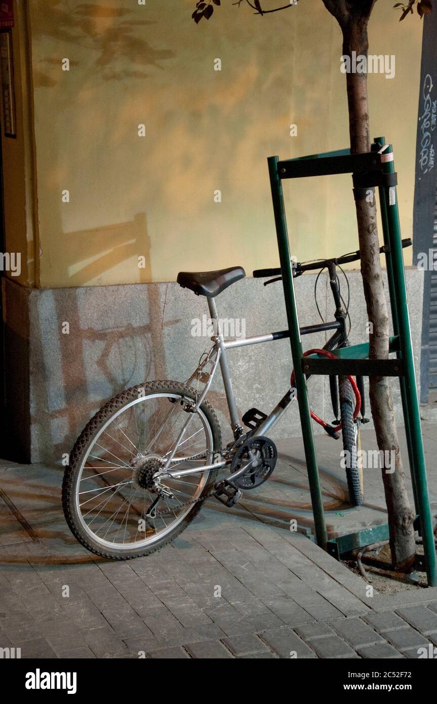 A bicycle locked to a tree barrier in Madrid, Spain, at night. Stock Photo